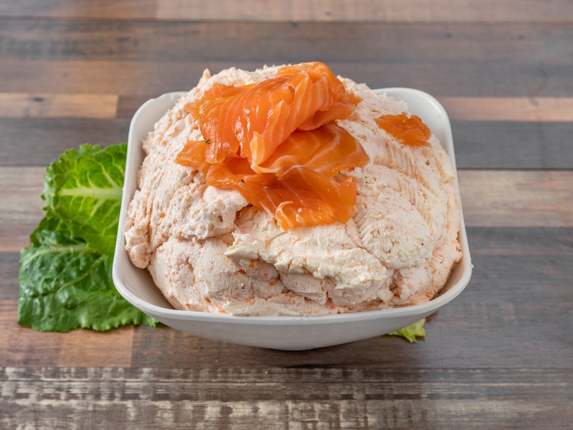 A bowl of mashed potatoes with smoked salmon on top on a wooden table.