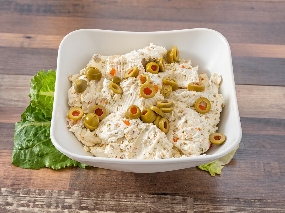 A white bowl filled with chicken and olives on a wooden table.