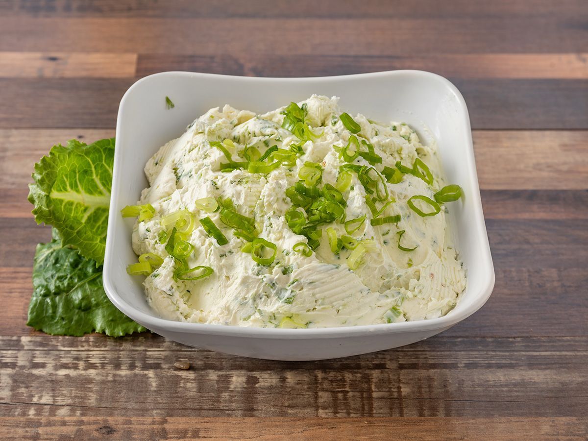 A bowl of mashed potatoes with green onions on a wooden table.