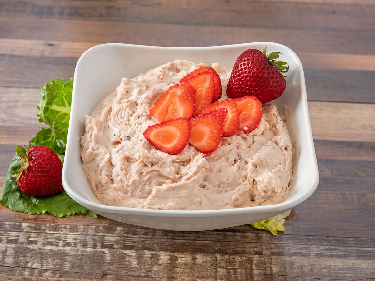 A bowl of strawberry dip with strawberries on top on a wooden table.
