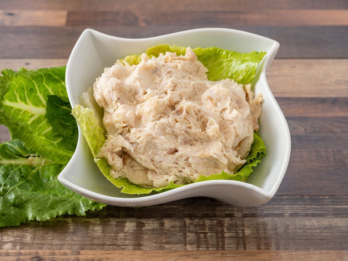 A white bowl filled with mashed potatoes and lettuce on a wooden table.