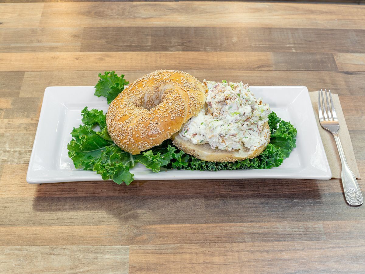 A bagel sandwich on a white plate with lettuce and a fork on a wooden table.