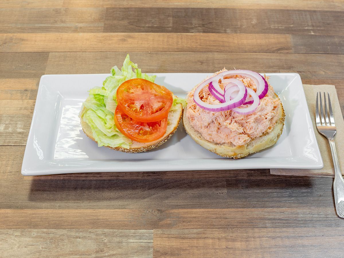 A sandwich with lettuce, tomatoes and onions on a bagel on a plate with a fork.