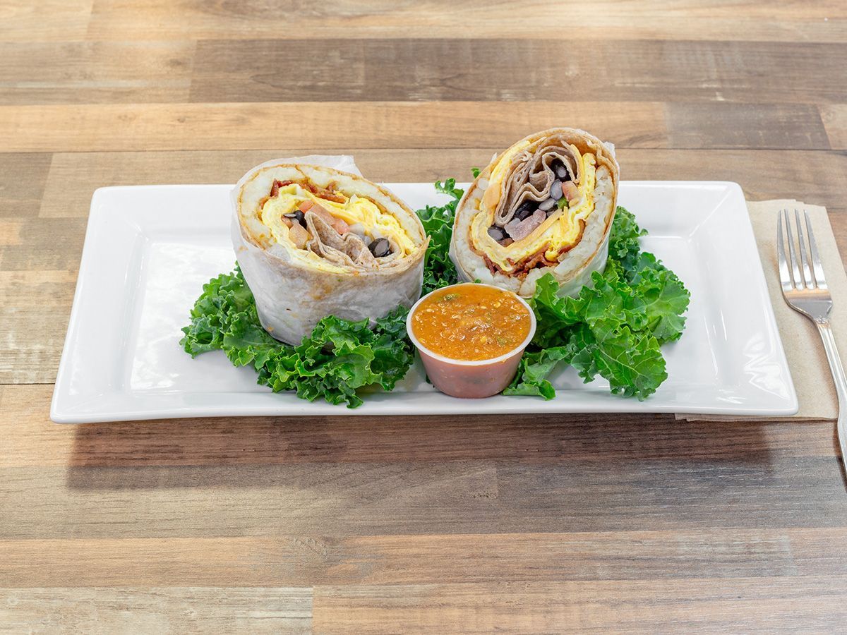 A white plate topped with a sandwich and a dipping sauce on a wooden table.