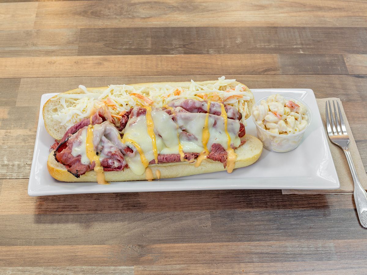 A sub sandwich with cheese and coleslaw on a white plate on a wooden table.