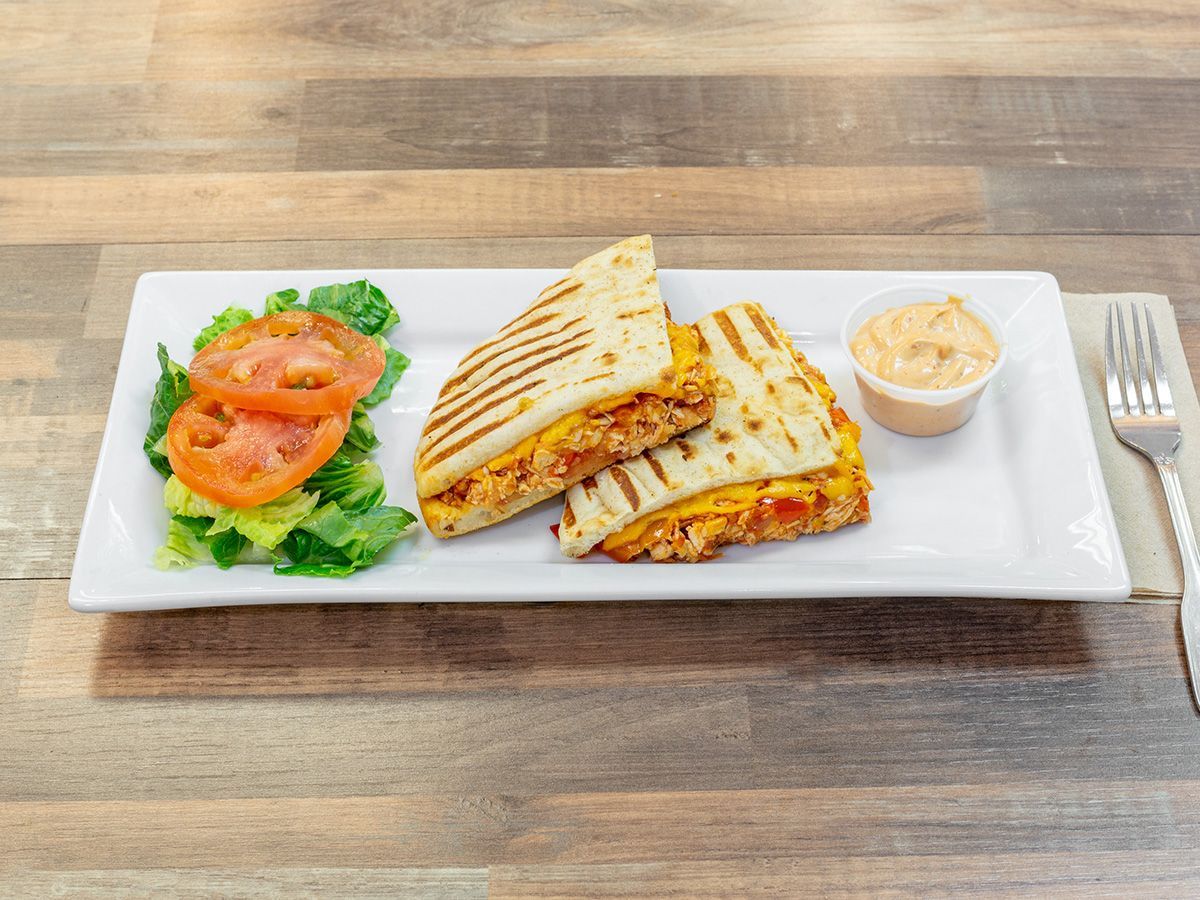 A sandwich with tomatoes and lettuce on a white plate on a wooden table.