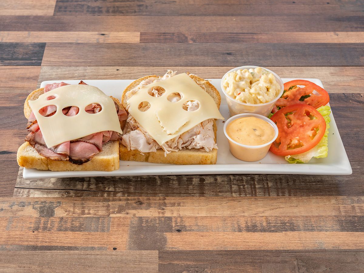 A sandwich with ham, cheese, turkey and tomatoes on a white plate on a wooden table.