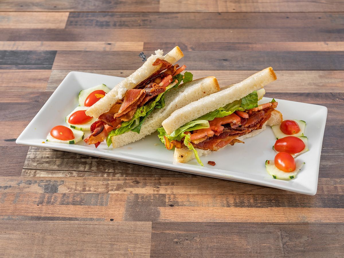 Two club sandwiches on a white plate on a wooden table.