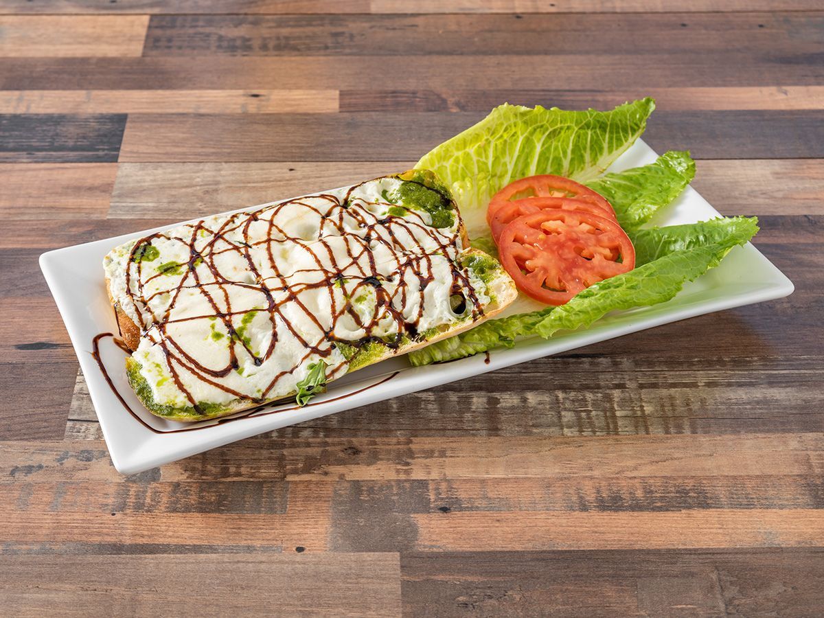 A sandwich with lettuce and tomato on a white plate on a wooden table.