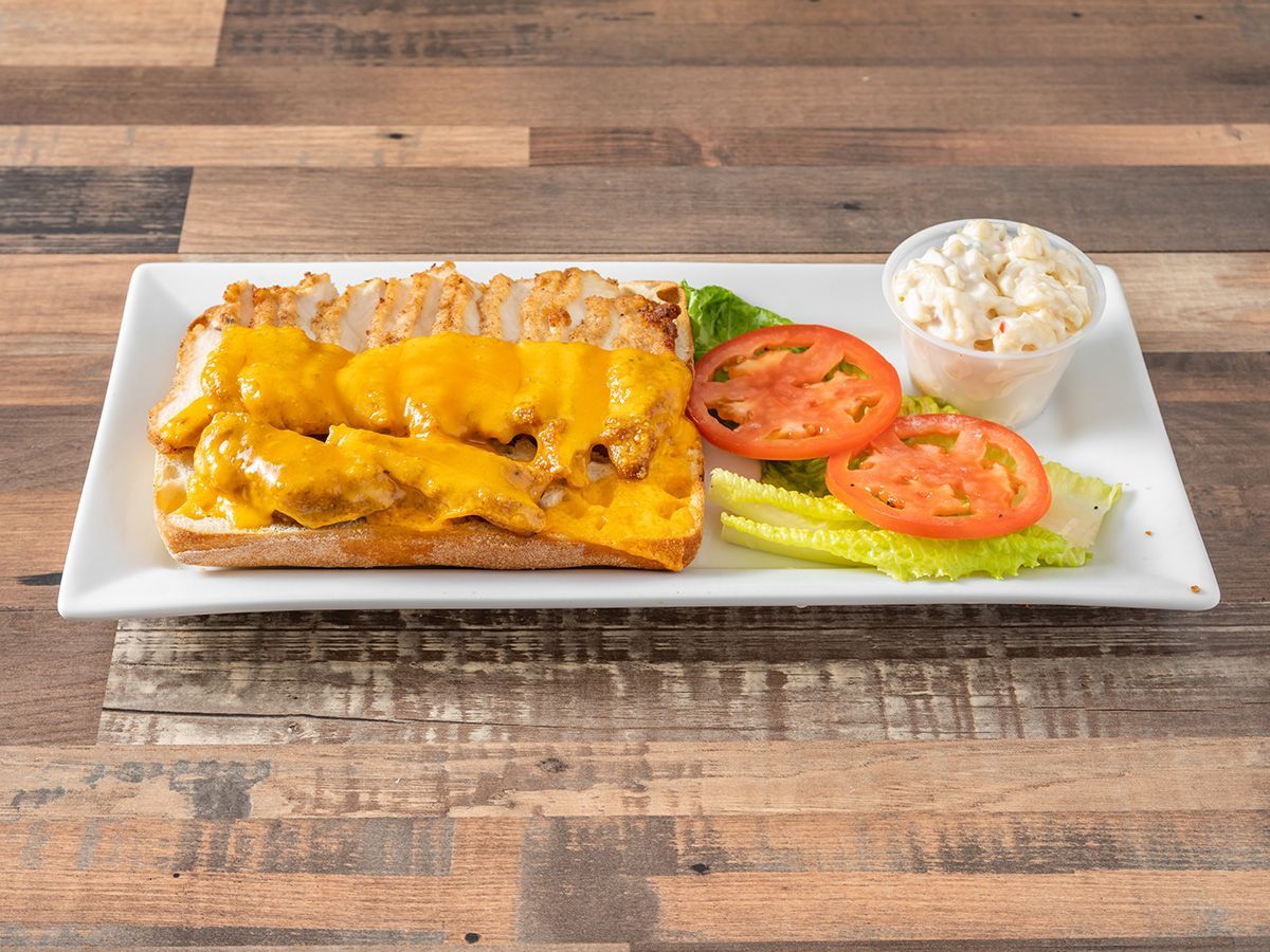 A sandwich with cheese, tomatoes, lettuce and coleslaw on a white plate on a wooden table.