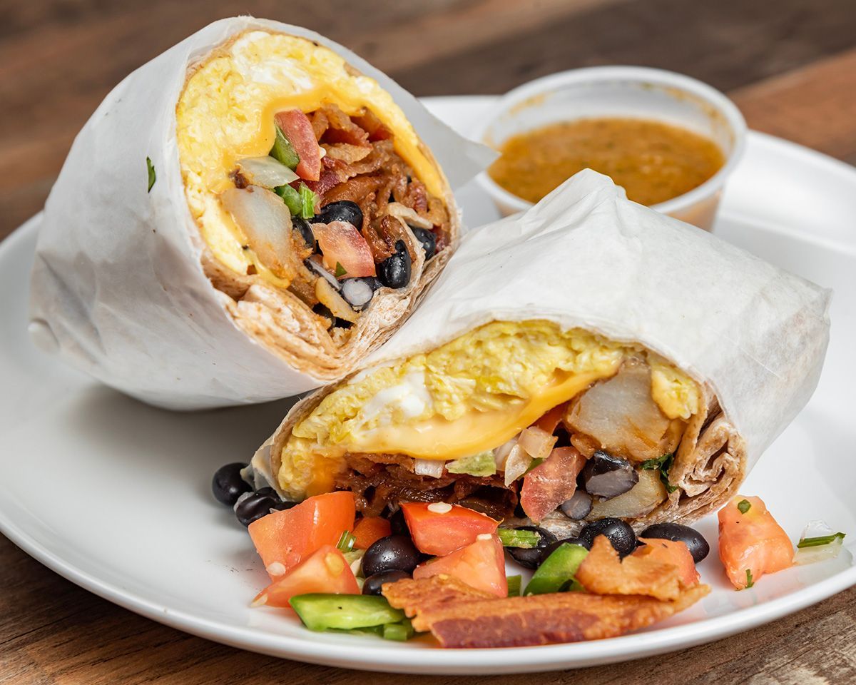 A burrito with eggs, bacon, black beans and tomatoes on a white plate.