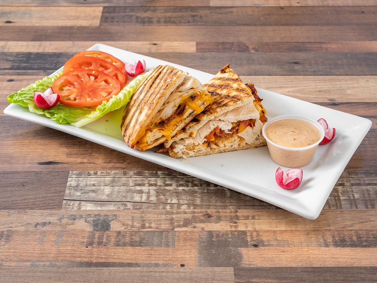 A sandwich with lettuce, tomatoes and radishes on a white plate on a wooden table.