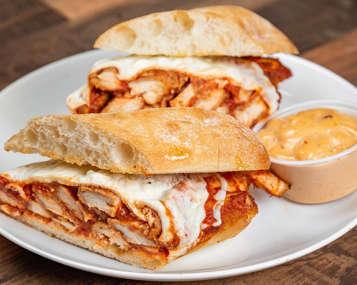 A chicken parmesan sandwich with french fries and dipping sauce on a plate.