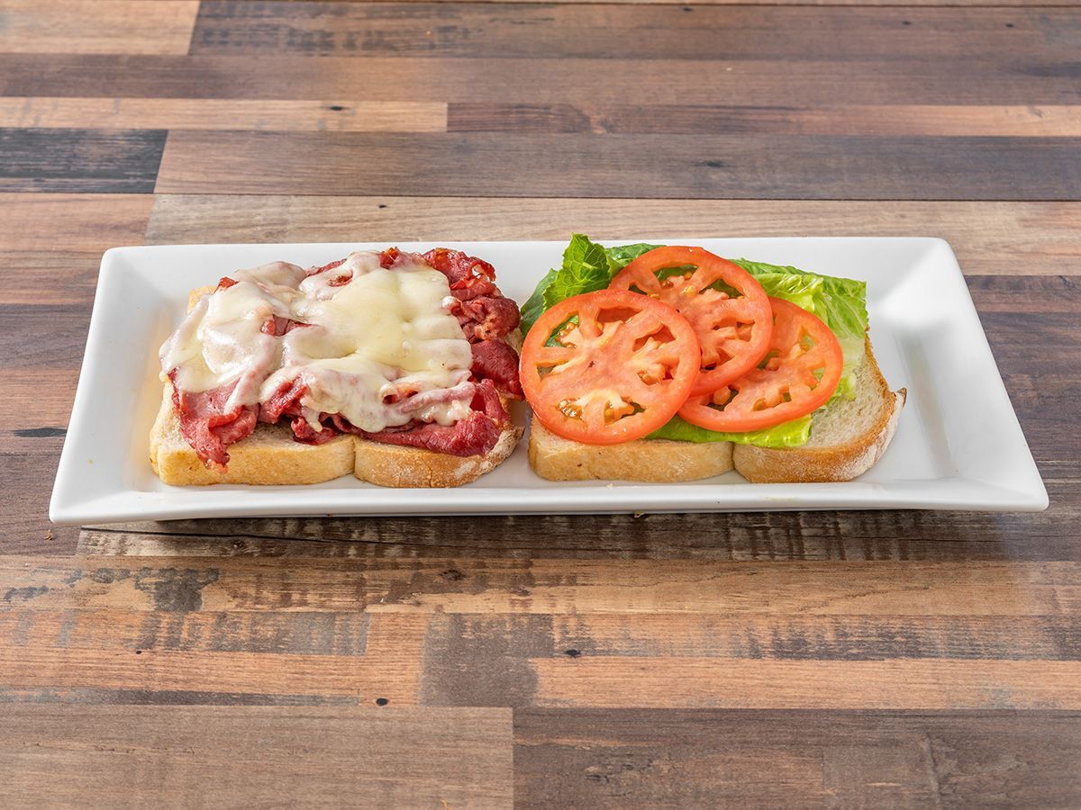 A sandwich with meat, cheese, lettuce and tomatoes on a white plate on a wooden table.