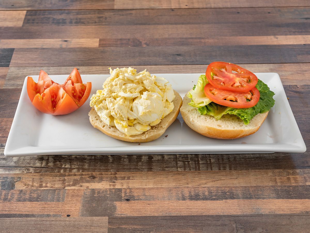 A sandwich with scrambled eggs, lettuce and tomatoes on a plate on a wooden table.