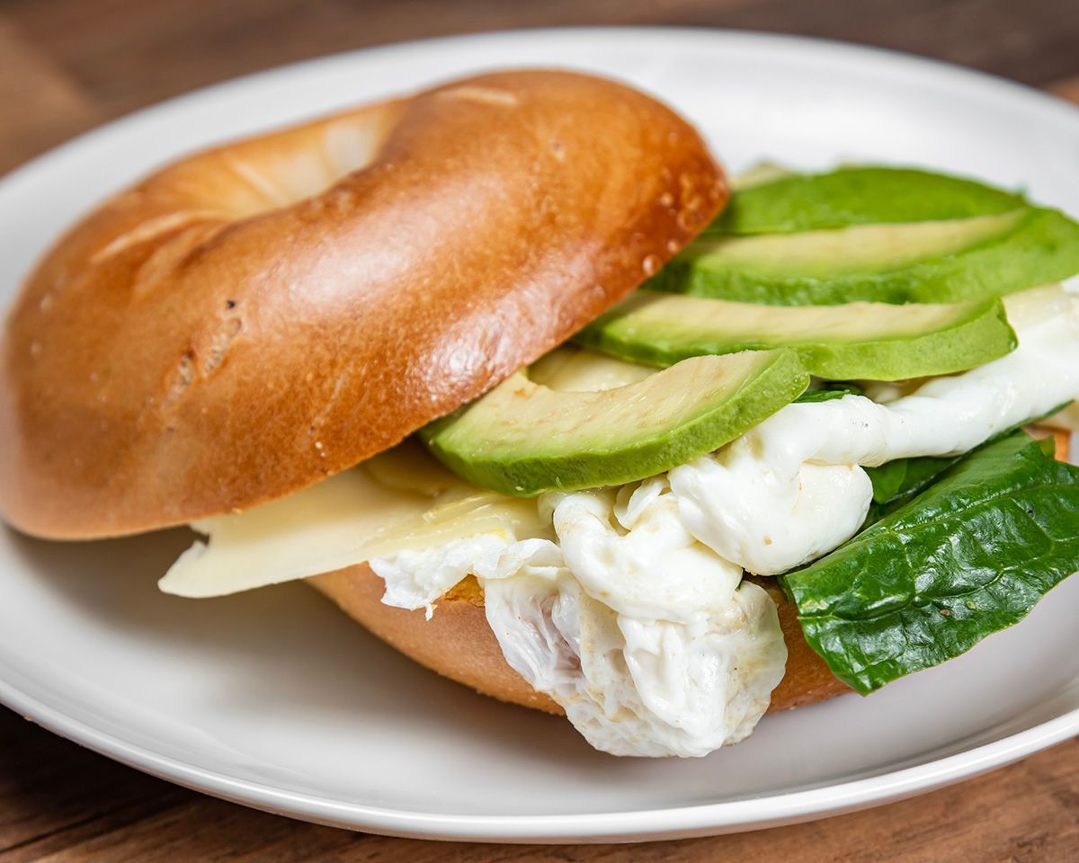 A bagel sandwich with avocado, egg, cheese and lettuce on a plate.