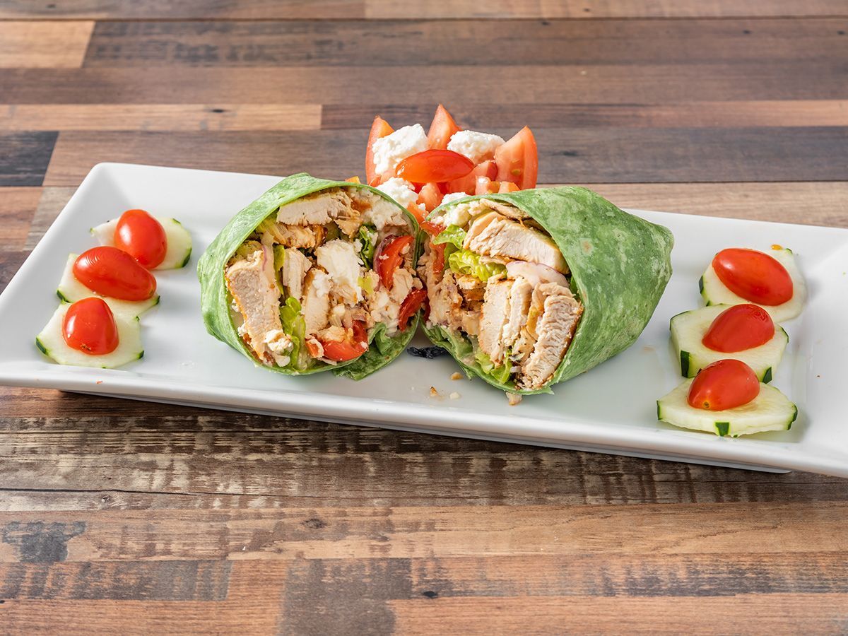 A chicken wrap with tomatoes and cucumbers on a white plate.