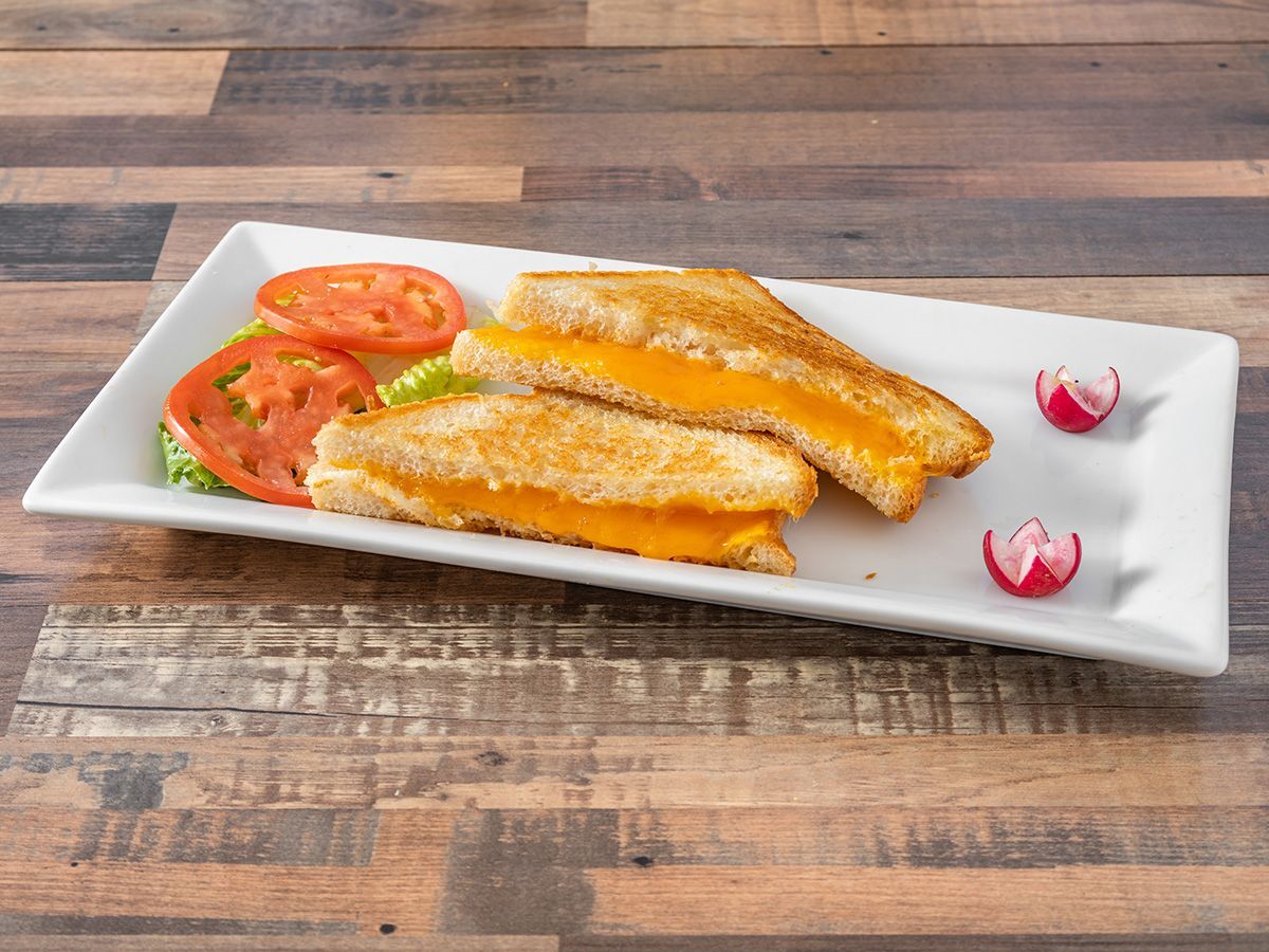 A grilled cheese sandwich with tomatoes and lettuce on a white plate on a wooden table.
