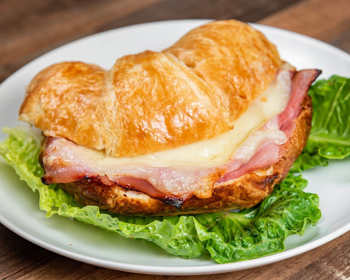 A ham and cheese sandwich on a croissant on a white plate.