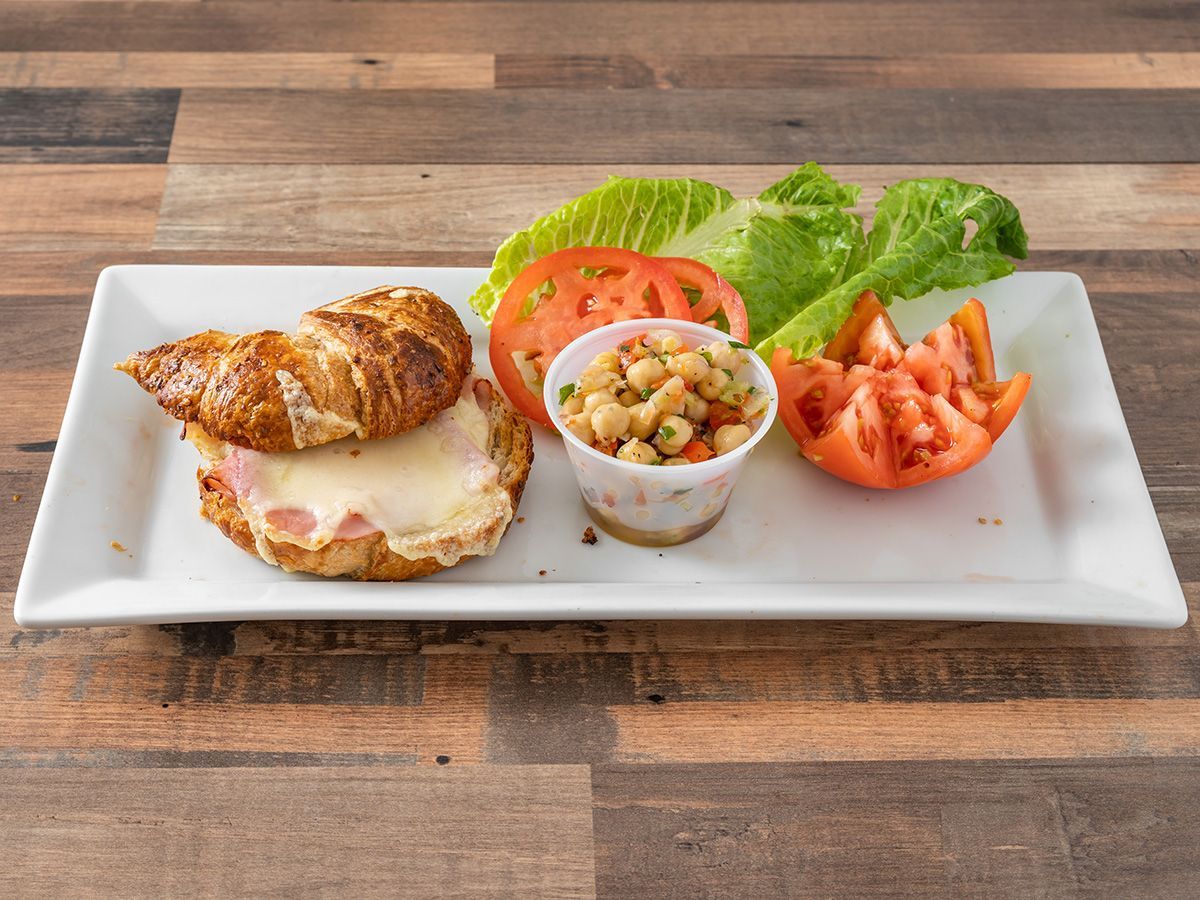 A white plate topped with a croissant sandwich, tomatoes, lettuce and beans.