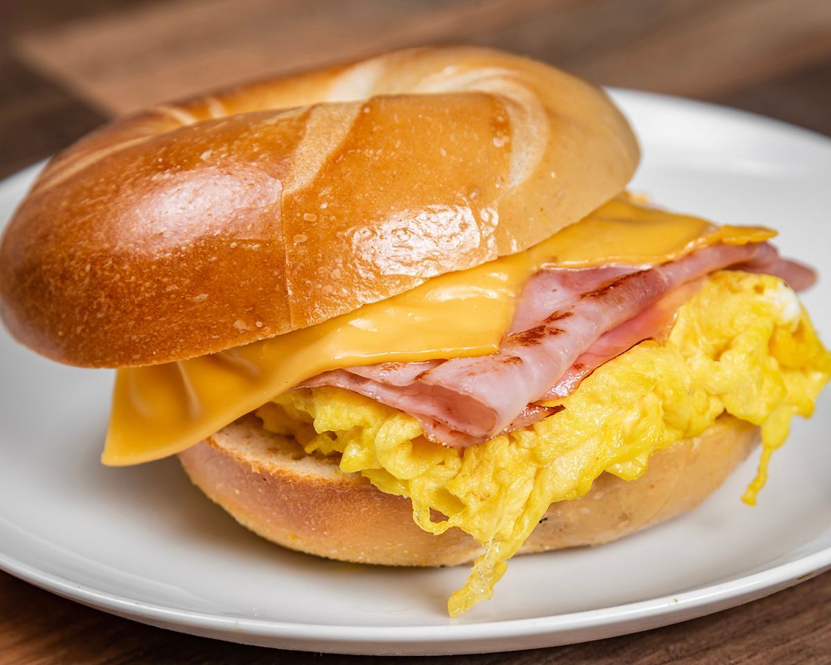 A bagel sandwich with ham and eggs on a white plate.