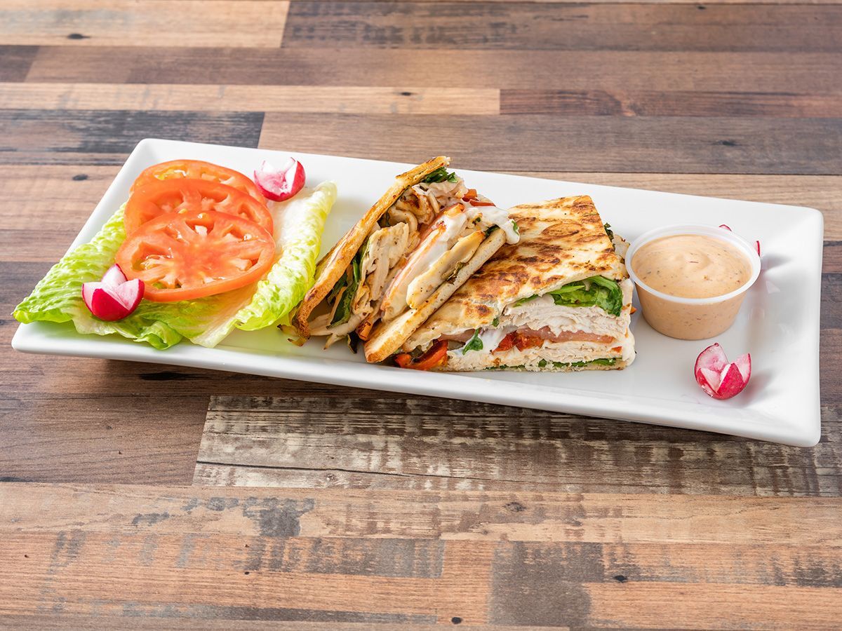 A sandwich with lettuce, tomatoes, and radishes on a white plate on a wooden table.