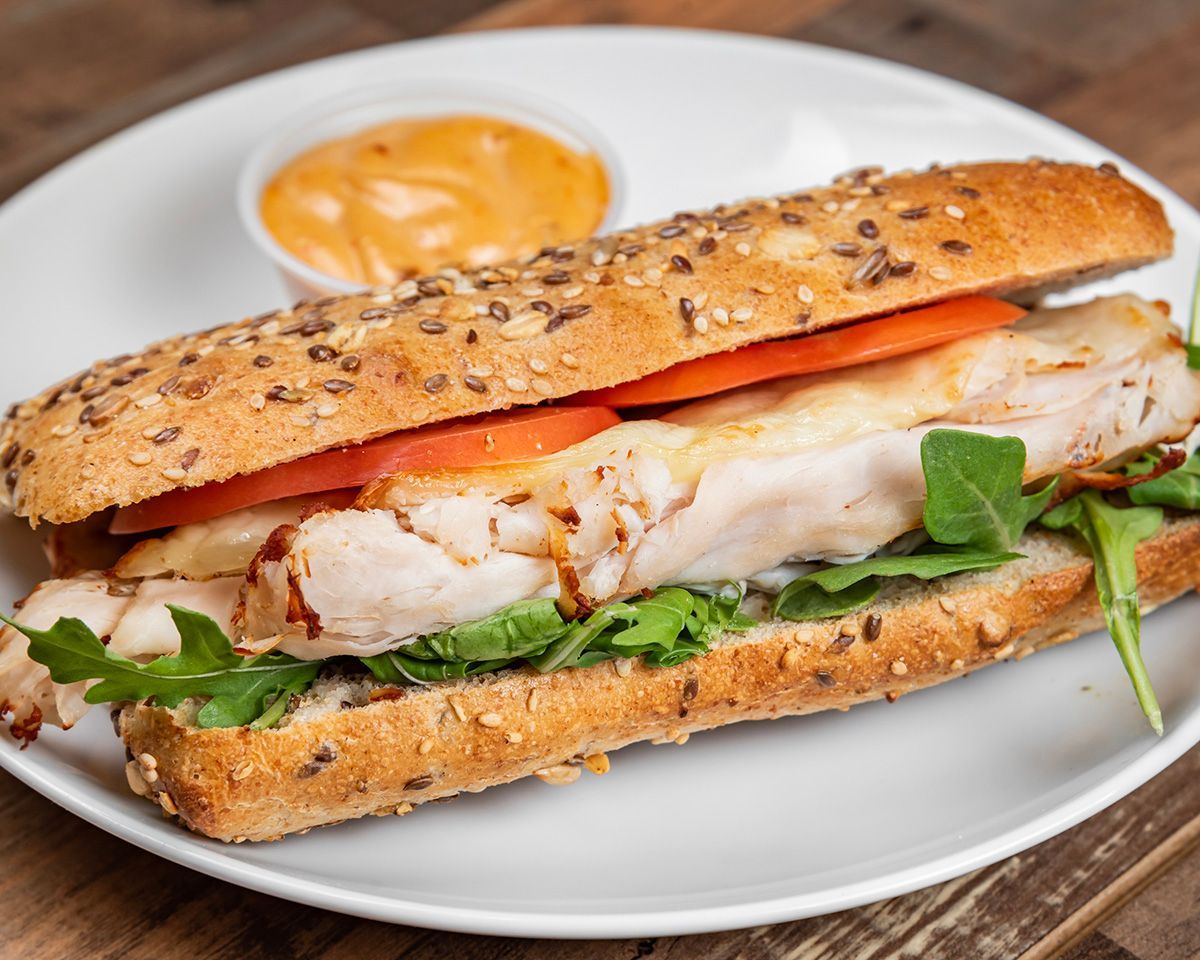 A sandwich with chicken, tomatoes, lettuce and cheese on a white plate.