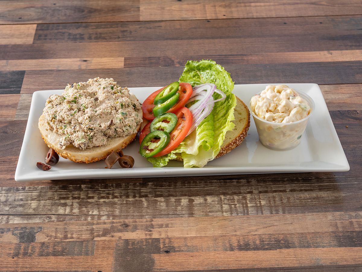A sandwich with lettuce, tomatoes, onions and mayonnaise on a white plate on a wooden table.
