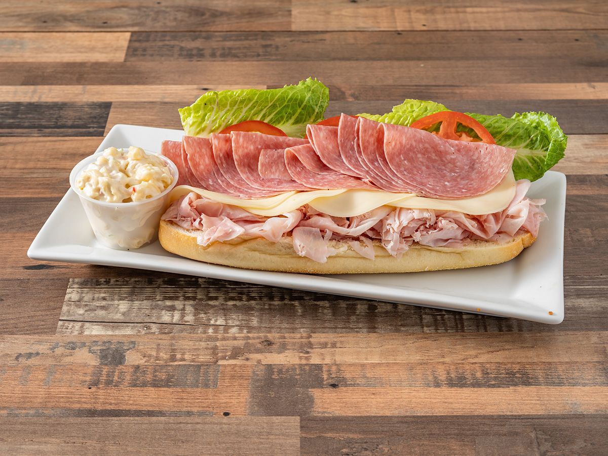 A sub sandwich with ham, cheese, lettuce and tomatoes on a white plate on a wooden table.
