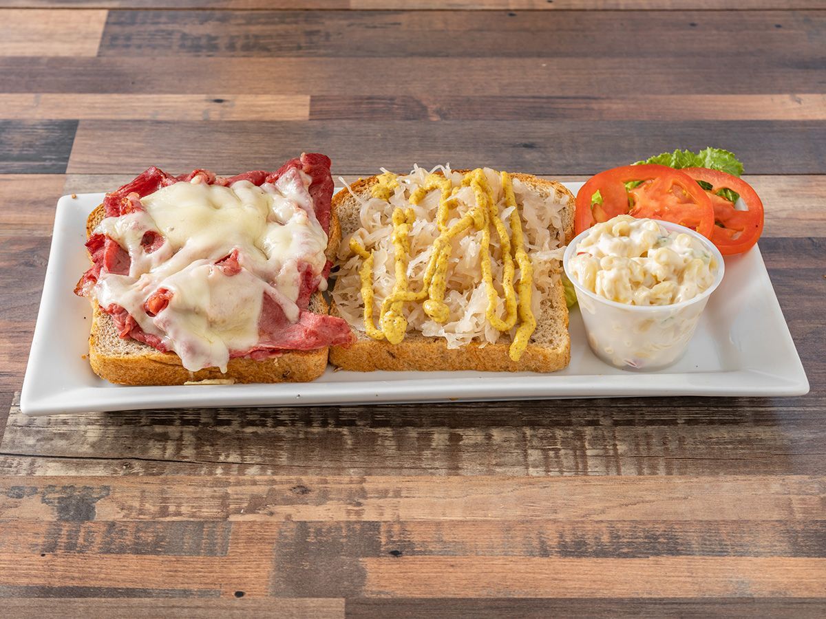 A plate of food with meat, cheese, mustard and tomatoes on a wooden table.
