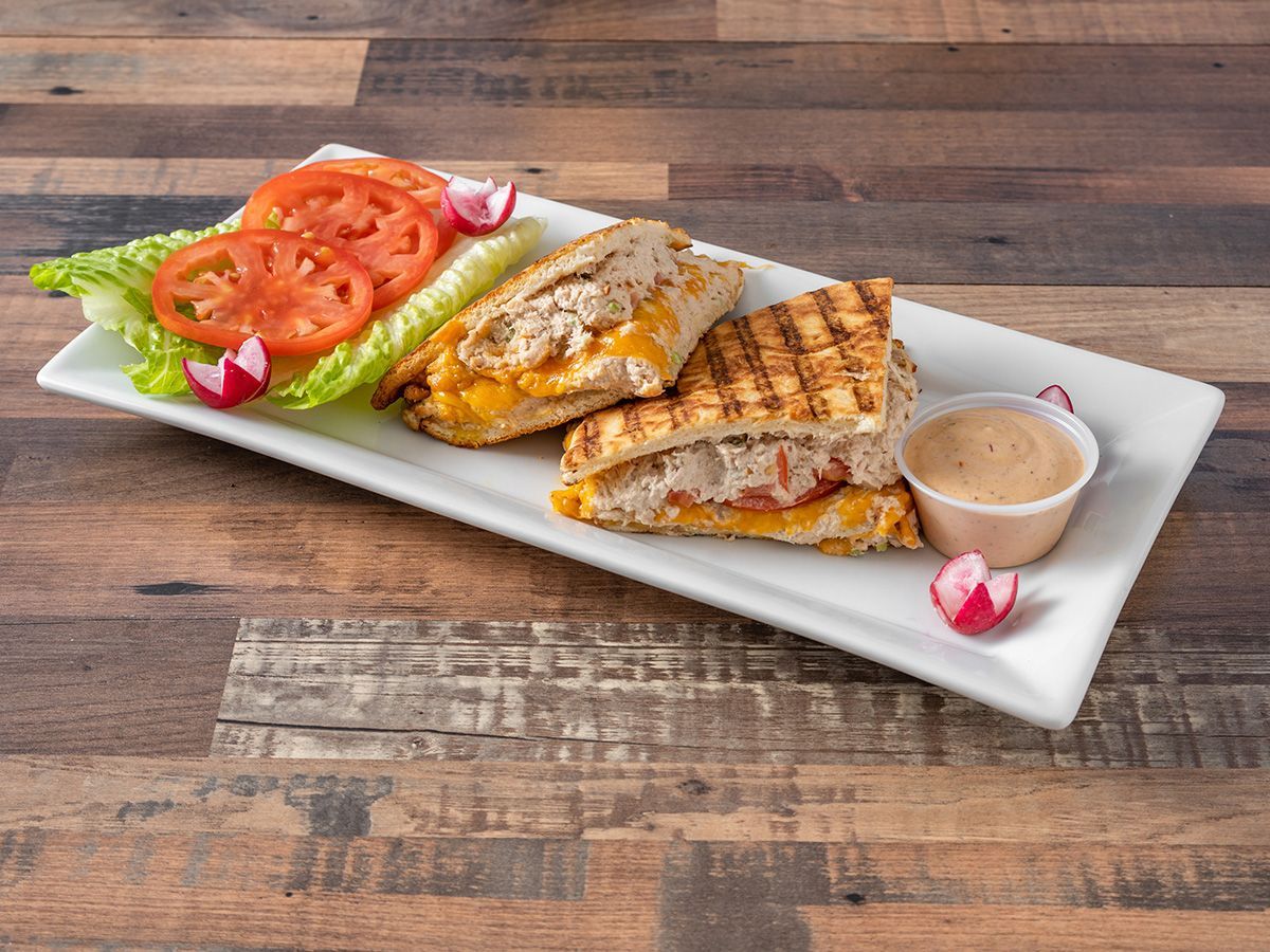 A grilled sandwich with lettuce and tomatoes on a white plate on a wooden table.