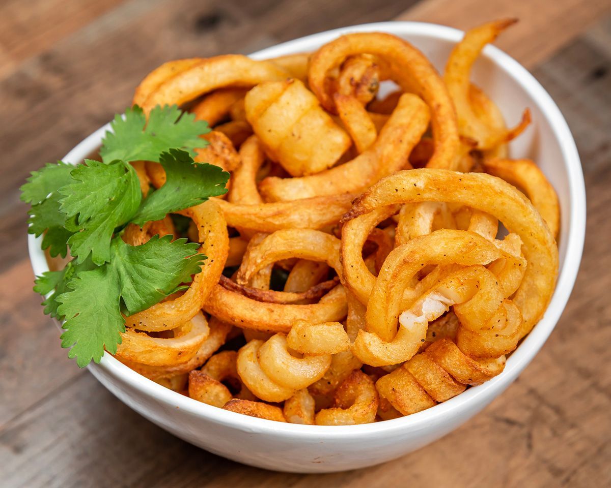 A bowl of curly fries with cilantro on a wooden table.