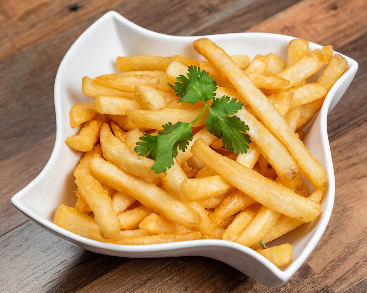 A bowl of french fries with parsley on a wooden table.