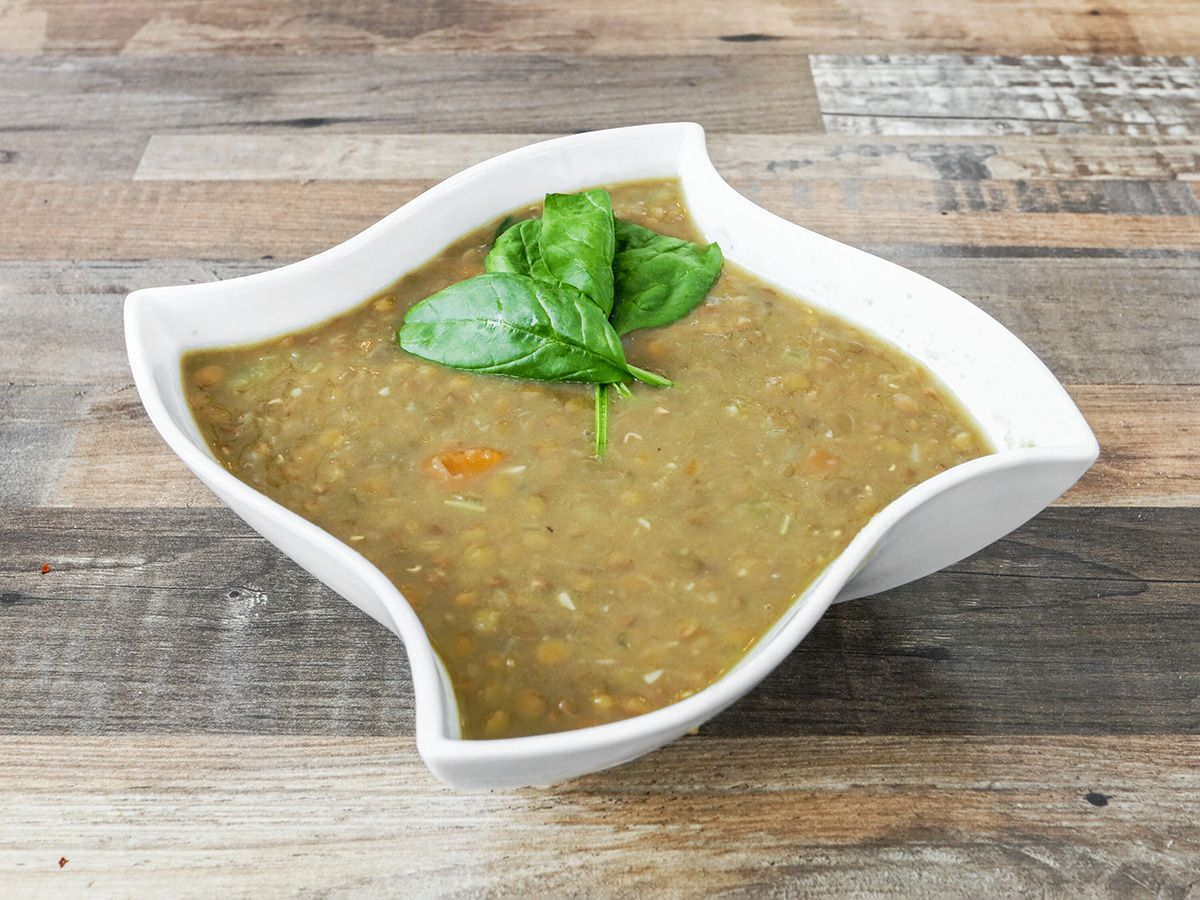A bowl of soup with basil on top is on a wooden table.