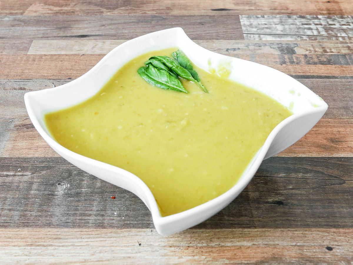 A bowl of soup with spinach on top on a wooden table.