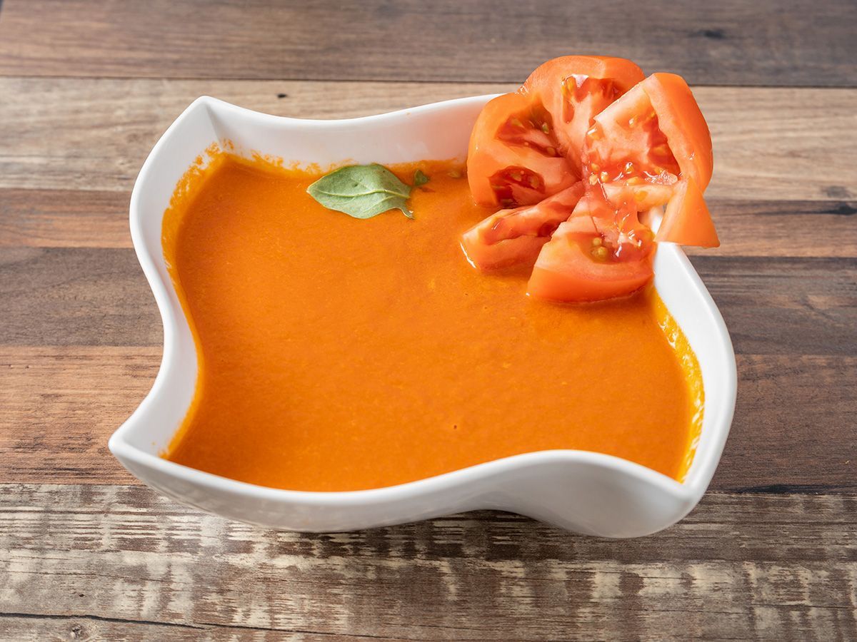 A bowl of tomato soup with tomatoes on top on a wooden table.