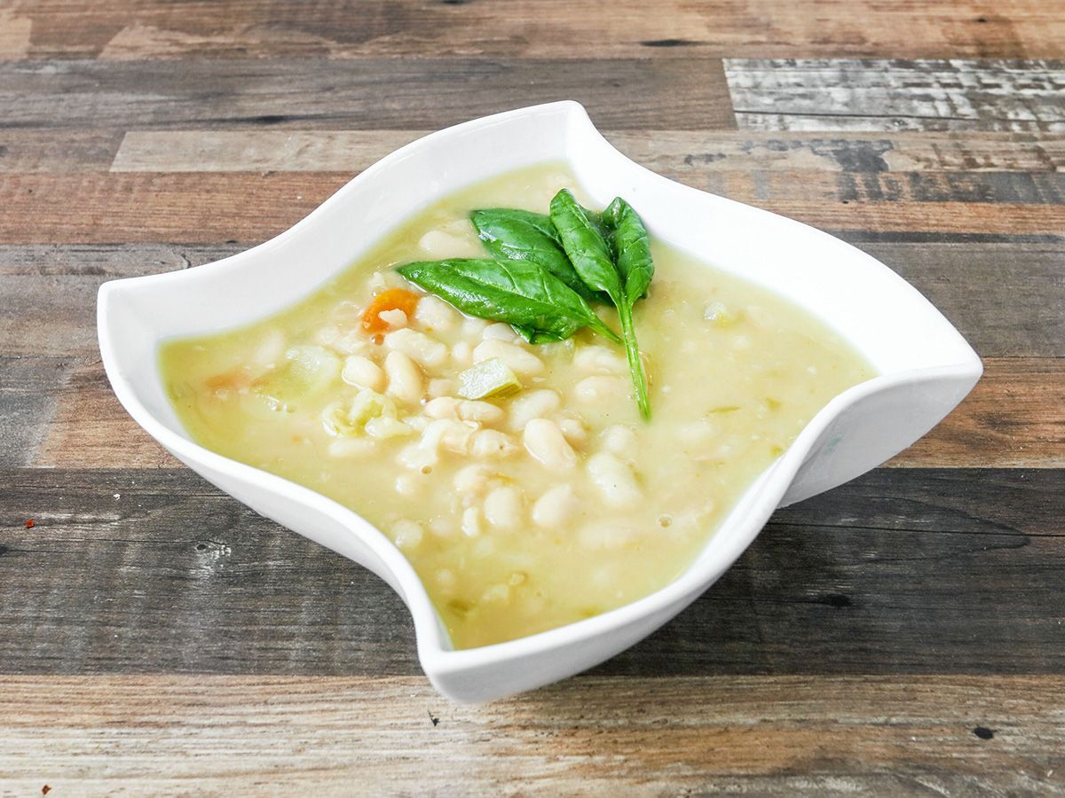 A bowl of soup with beans and carrots on a wooden table.