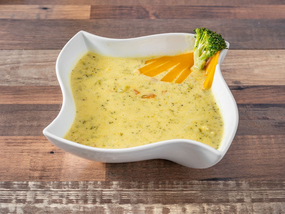 A bowl of soup with broccoli and carrots on a wooden table.
