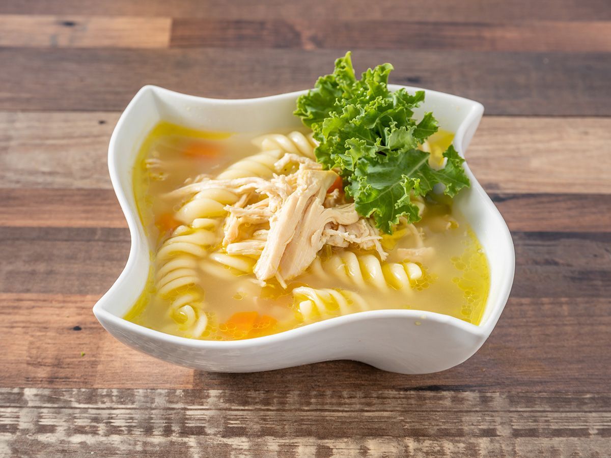 A bowl of chicken noodle soup with lettuce on a wooden table.
