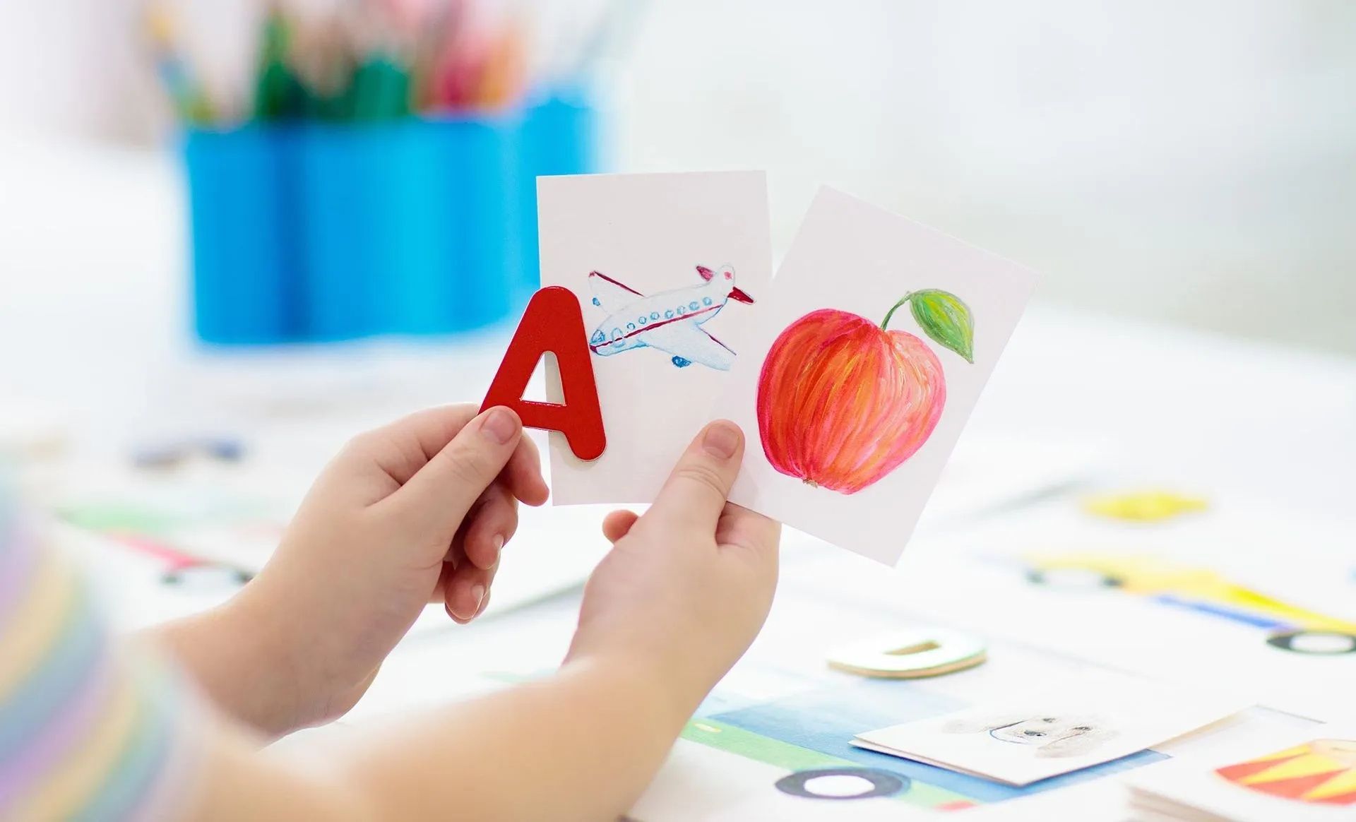 A child is holding a card with the letter a and an apple on it.