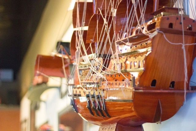 Close-up of a wooden model sailing ship with detailed rigging and orange sails on display