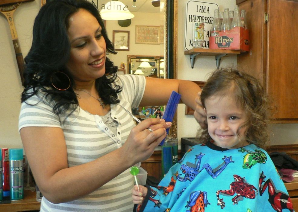Woman giving a child a haircut in a salon chair
