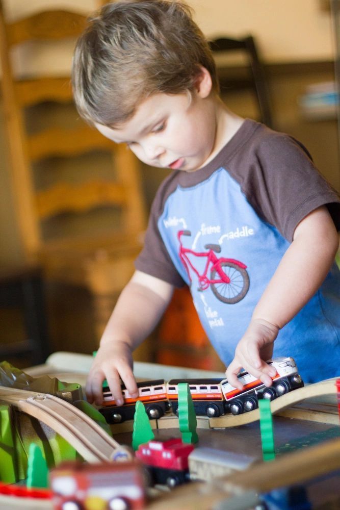 Child playing with a toy train set at a table, looking down while arranging the tracks.