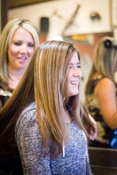 Woman smiling in a salon chair while a stylist stands behind her with a mirror in the background
