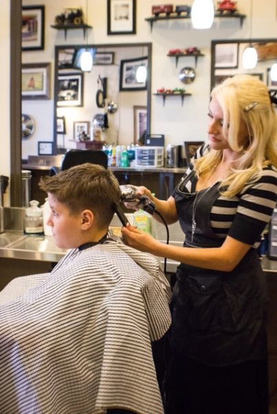 Hairdresser cutting a client’s hair in a barbershop, with mirrors and framed photos in the background