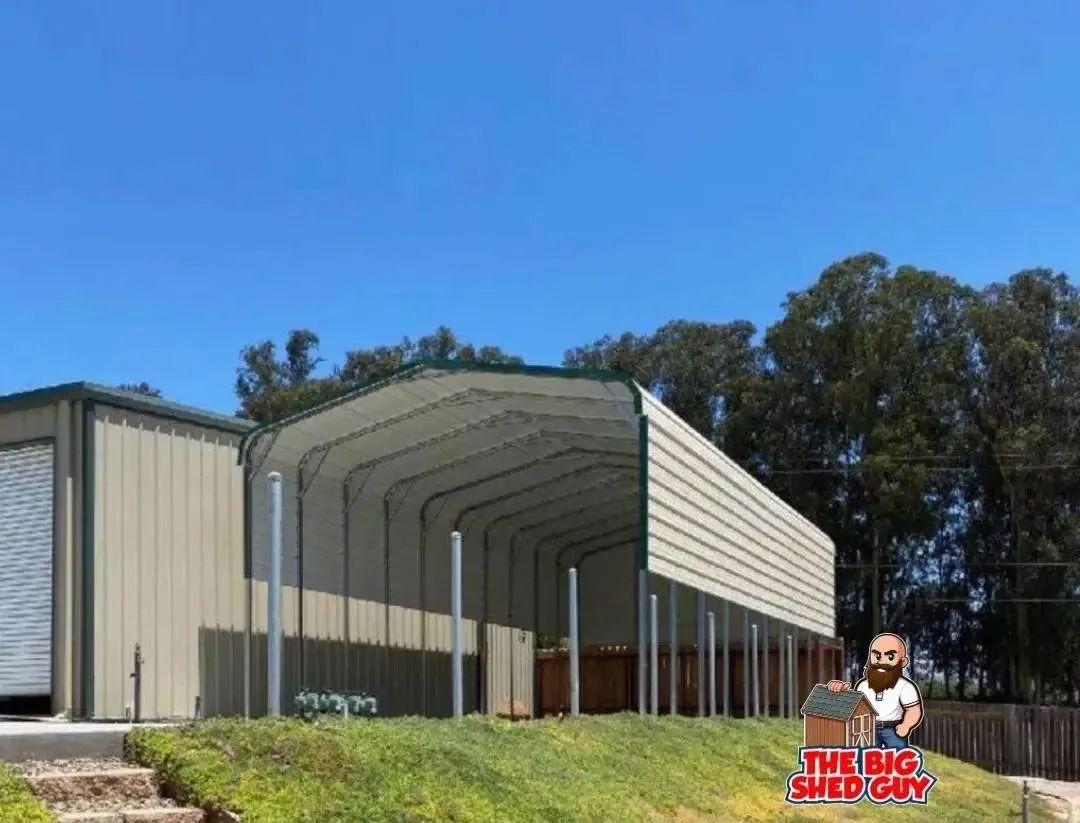 Metal carport and storage building on a grassy hill under a blue sky.