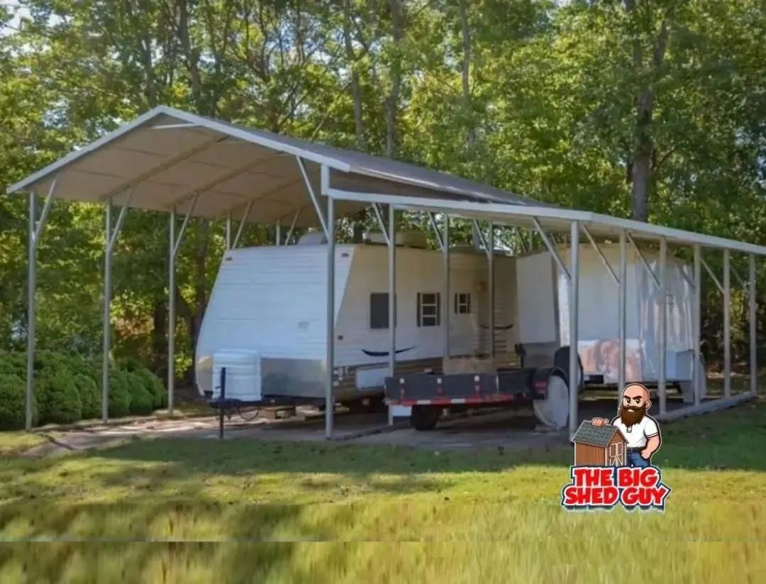 A white RV trailer parked under a metal carport in a grassy area with trees.