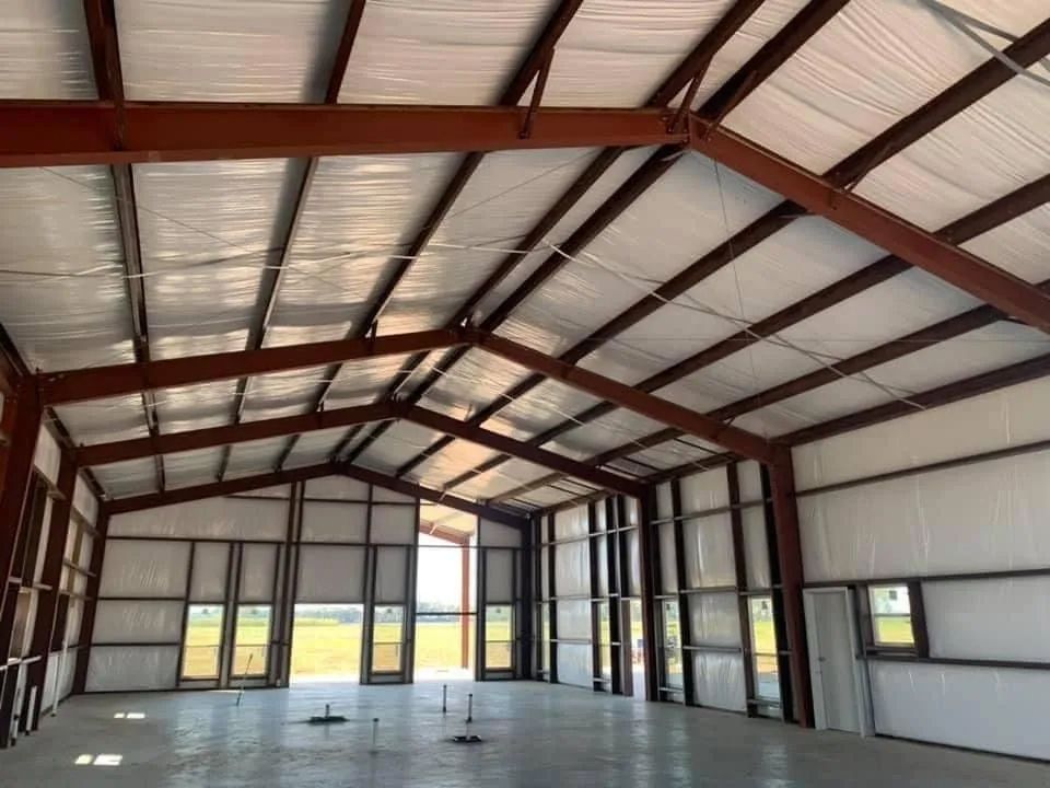 Interior of a large steel-framed building with a high ceiling, windows, and concrete floor.