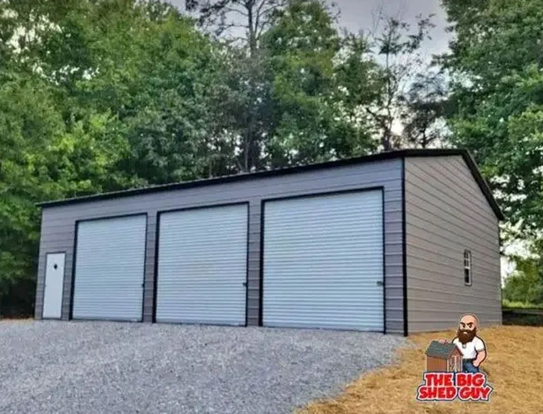Three-bay gray metal garage with roll-up doors, gravel driveway, and a small side door.