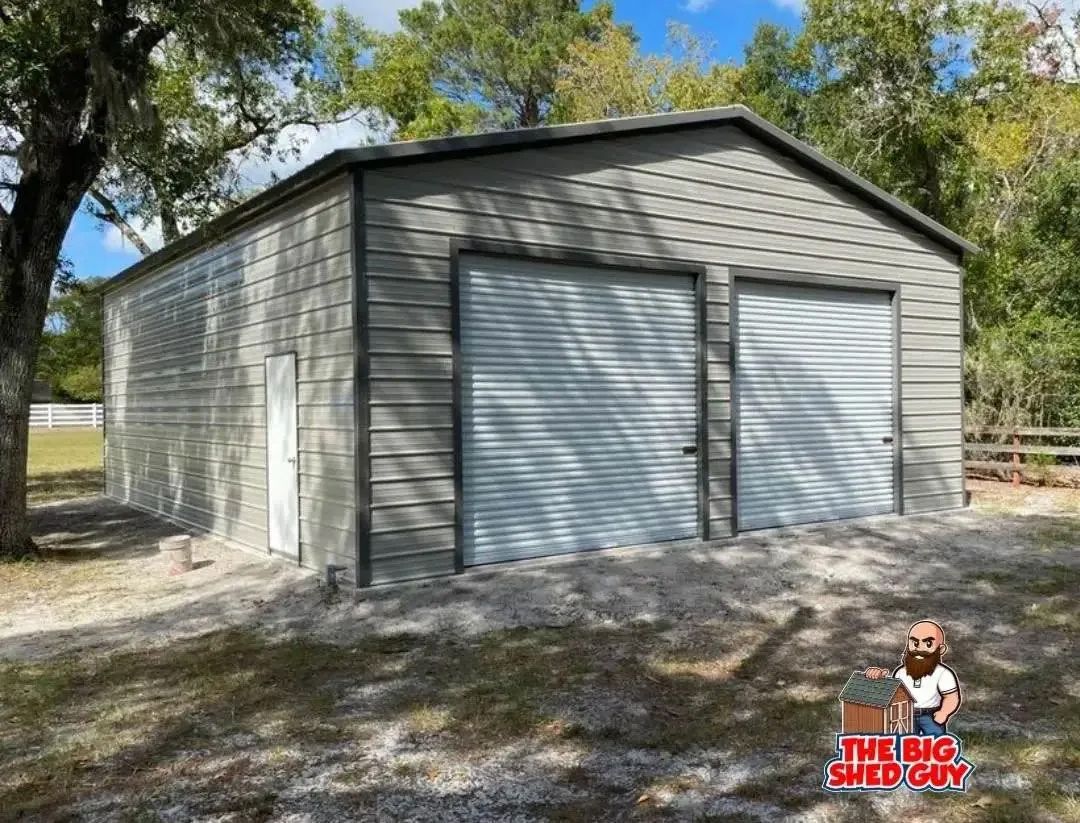 Gray metal garage with two roll-up doors, a side door, and gravel base outdoors.